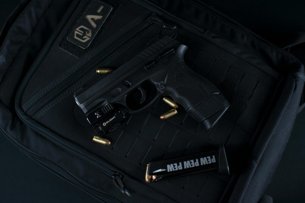 A compact handgun with a mounted light, surrounded by ammunition, placed on a black tactical bag.